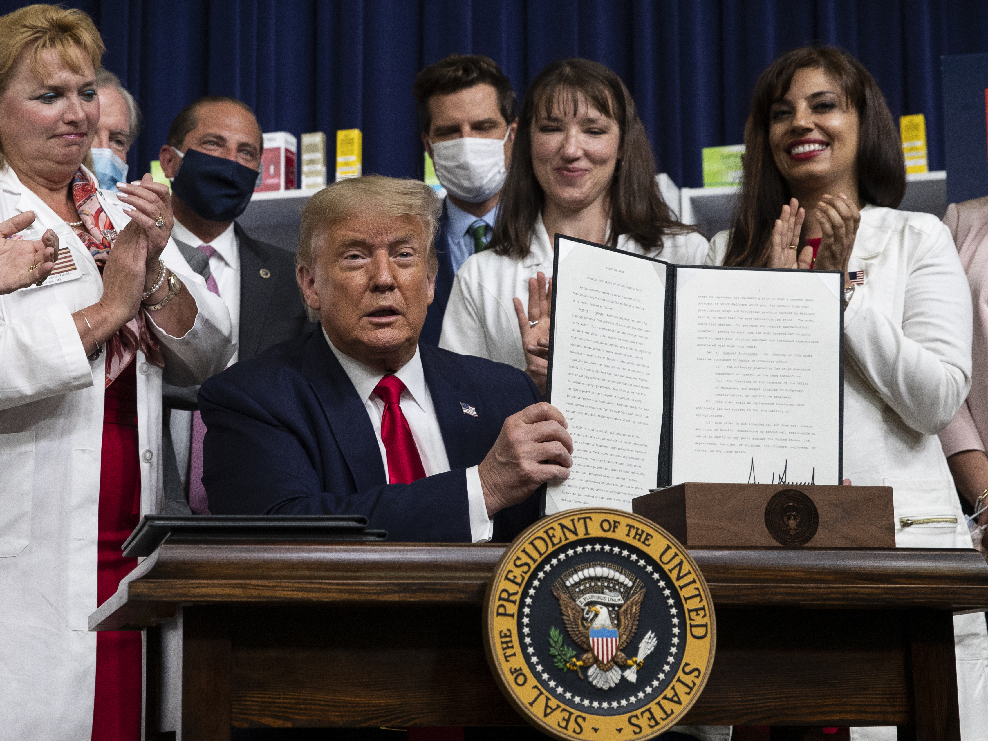 caption: President Trump holds up a signed executive order on lowering drug prices on July 24.