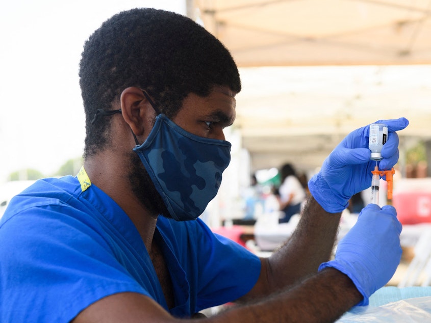 caption: A health care worker prepares a dose of the Moderna COVID-19 vaccine during a clinic held at the Watts Juneteenth Street Fair in the Watts neighborhood of Los Angeles.