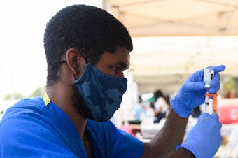 caption: A health care worker prepares a dose of the Moderna COVID-19 vaccine during a clinic held at the Watts Juneteenth Street Fair in the Watts neighborhood of Los Angeles.