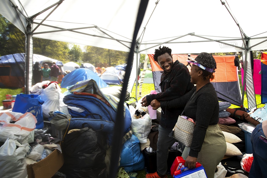 caption: Migrants from Angola and The Democratic Republic of the Congo laugh together inside a tent with various supplies on Wednesday, May 1, 2024, at Powell Barnett Park in Seattle. Unsheltered migrants have set up an encampment at the park. 