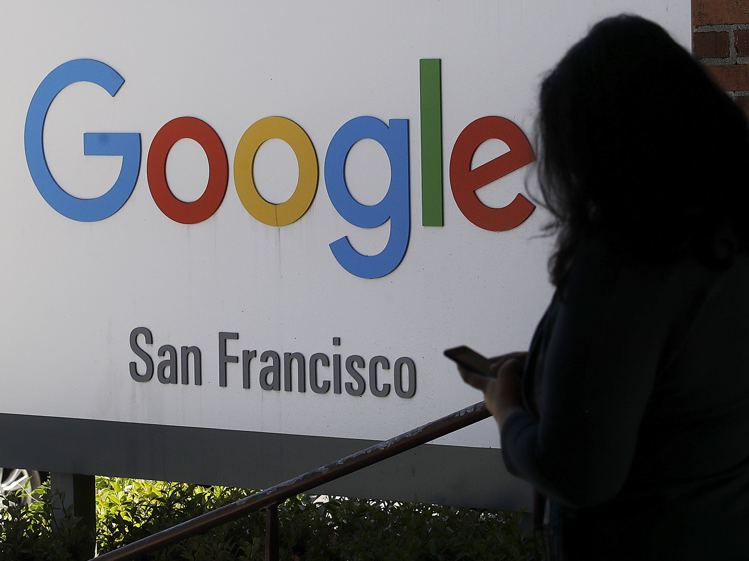 caption: A woman walks past a Google sign in San Francisco. The Justice Department is launching an antitrust review of major online companies. The DOJ did not name the firms, but there have been increasing calls to regulate companies like Google, Facebook and Amazon.