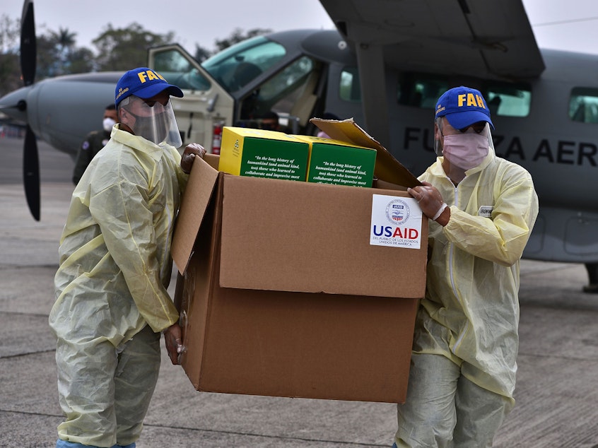 caption: Foreign aid takes many forms — and Trump and Biden have differing perspectives. Above: Members of the Honduran Armed Forces carry a box of COVID-19 diagnostic testing kits donated by the United States Agency for International Development and the International Organization for Migration.