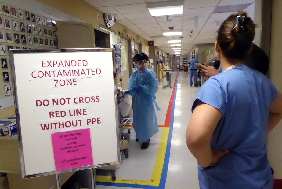 caption: A view of the entrance of the Covid ICU at University of Washington Medical Center on April 24, 2020. Amy Haverland, the nurse manager, is on the right. The taped red line down the middle of the aisle indicates where only medical staff with protective gear may go.