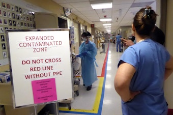 caption: A view of the entrance of the Covid ICU at University of Washington Medical Center on April 24, 2020. Amy Haverland, the nurse manager, is on the right. The taped red line down the middle of the aisle indicates where only medical staff with protective gear may go.