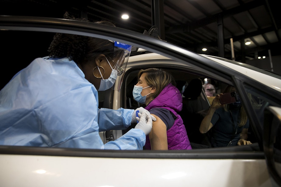 caption: Tamara Bass, a medical assistant at Neighborcare Health, left, administers the first dose of the Moderna Covid-19 vaccine for Neighborcare Physician Lisa Sferra on Thursday, January 7, 2021, at a drive-thru vaccination clinic for healthcare workers in Renton. 