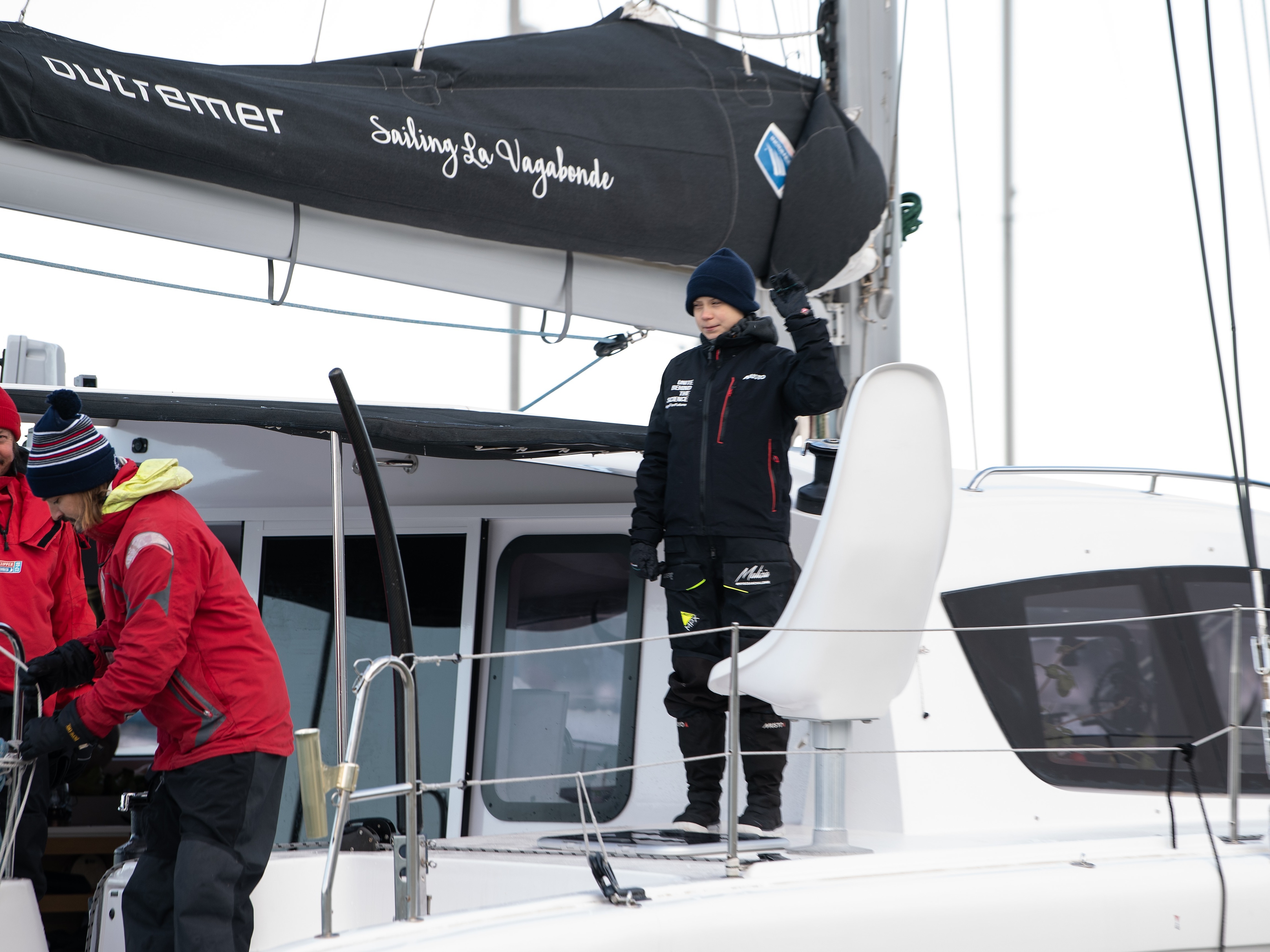 caption: Swedish climate activist Greta Thunberg waves aboard the catamaran La Vagabonde as she sets sail for Europe from Hampton, Va., on Wednesday.