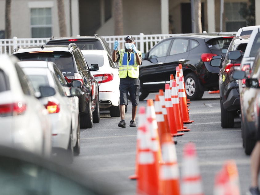 caption: A public safety officer directs drivers where to go last week at a coronavirus testing site at the Lee Davis Community Resource Center in Tampa, Fla.