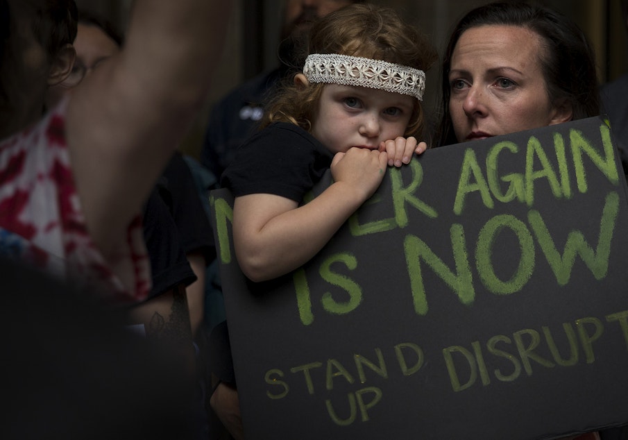 caption: Gloria Dykstra and Pearl Dykstra, 4, join hundreds of others in protest, holding a sign that reads 'Never Again is Now, Stand up and Disrupt,' outside of Seattle's downtown ICE offices on Thursday, August 8, 2019, on 2nd Avenue in Seattle. 