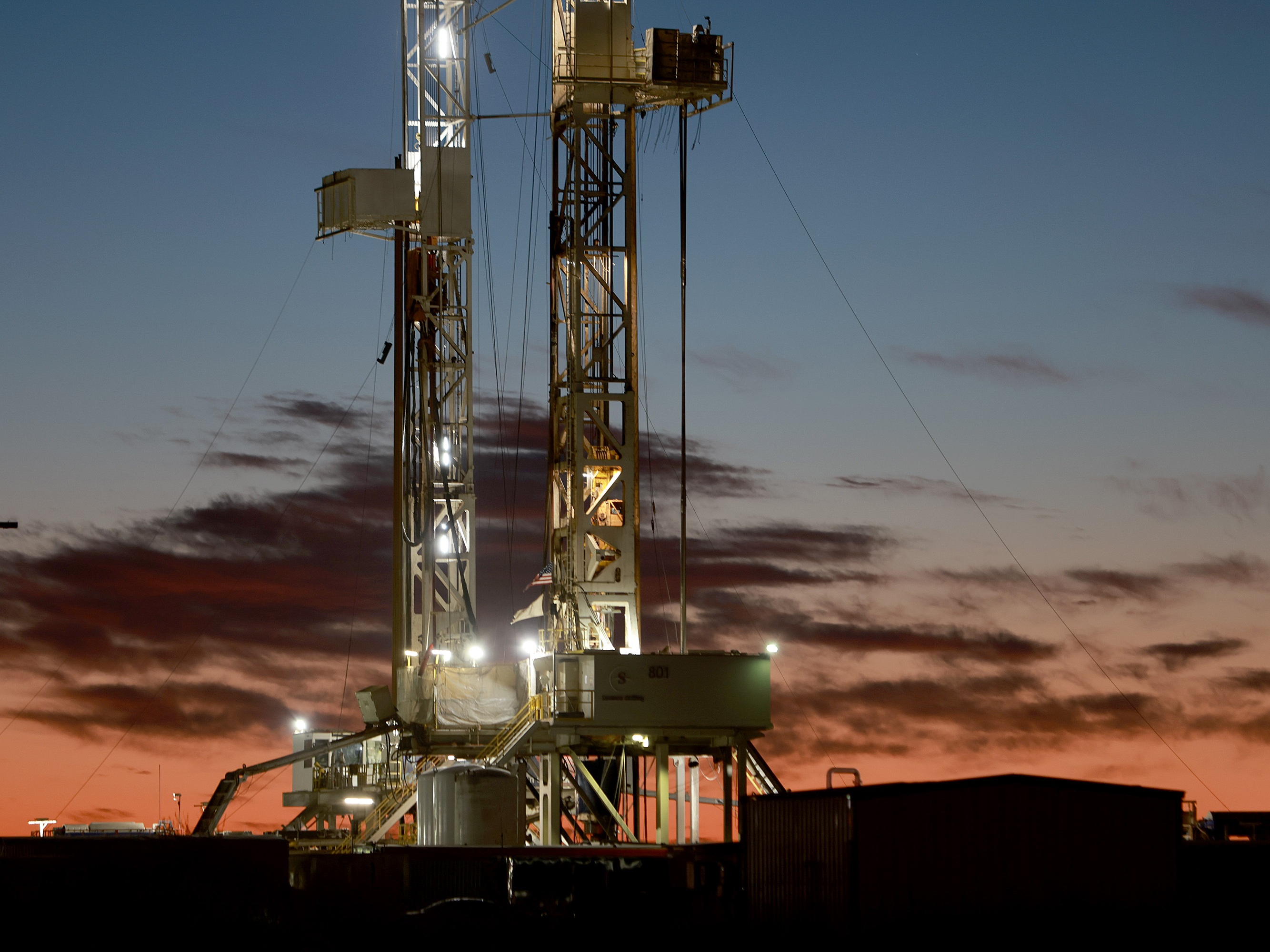 caption: An oil drilling rig in the Permian Basin on March 13, 2022, in Midland, Texas.