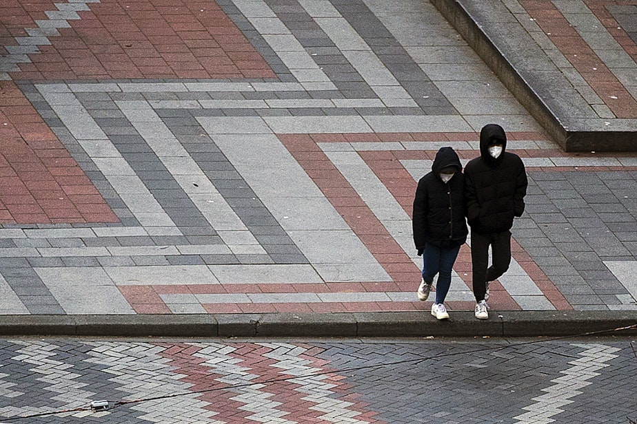 caption: Two people wearing masks cross 4th Avenue while walking along Pine Street on Tuesday, March 24, 2020, in Seattle.