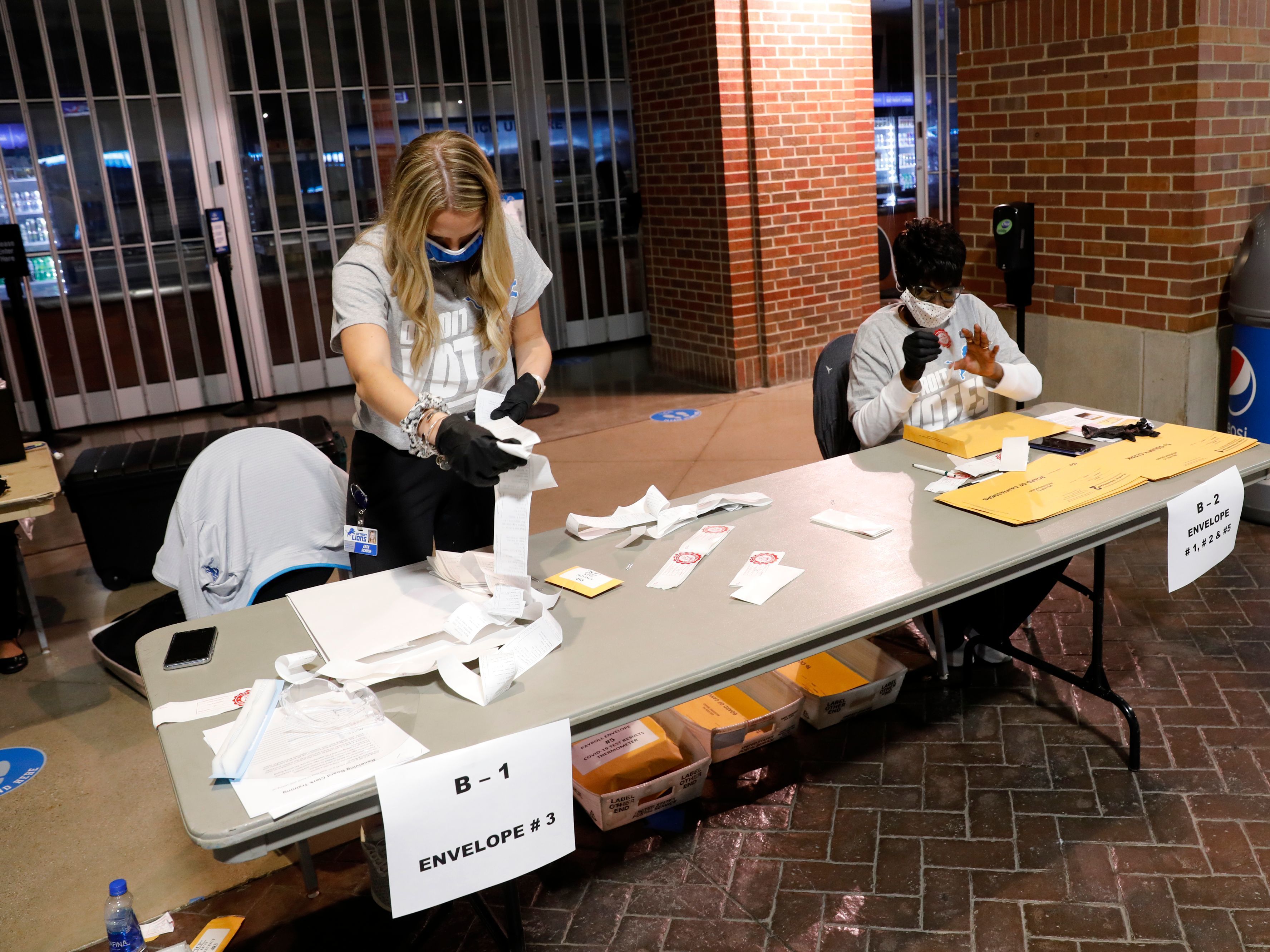 caption: Election workers check the tapes from the voting machines to verify they contain the correct signatures from polling stations after polls closed in the general election at Ford Field on November 3, 2020 in Detroit.