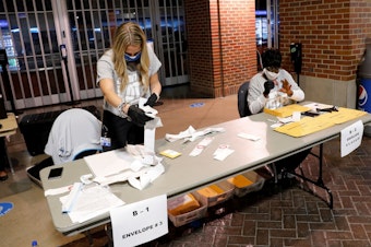 caption: Election workers check the tapes from the voting machines to verify they contain the correct signatures from polling stations after polls closed in the general election at Ford Field on November 3, 2020 in Detroit.