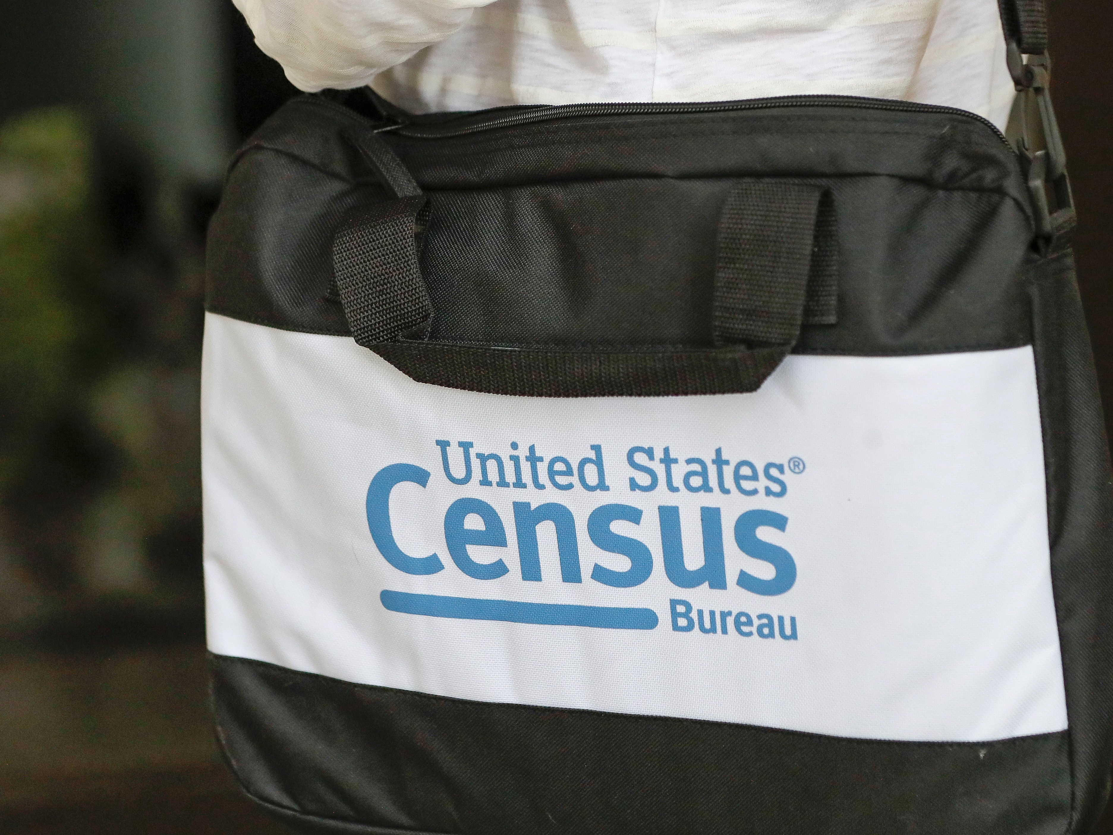 caption: The U.S. Census Bureau's logo is featured on a black bag carried by a census worker knocking on doors in 2020 in Winter Park, Florida.