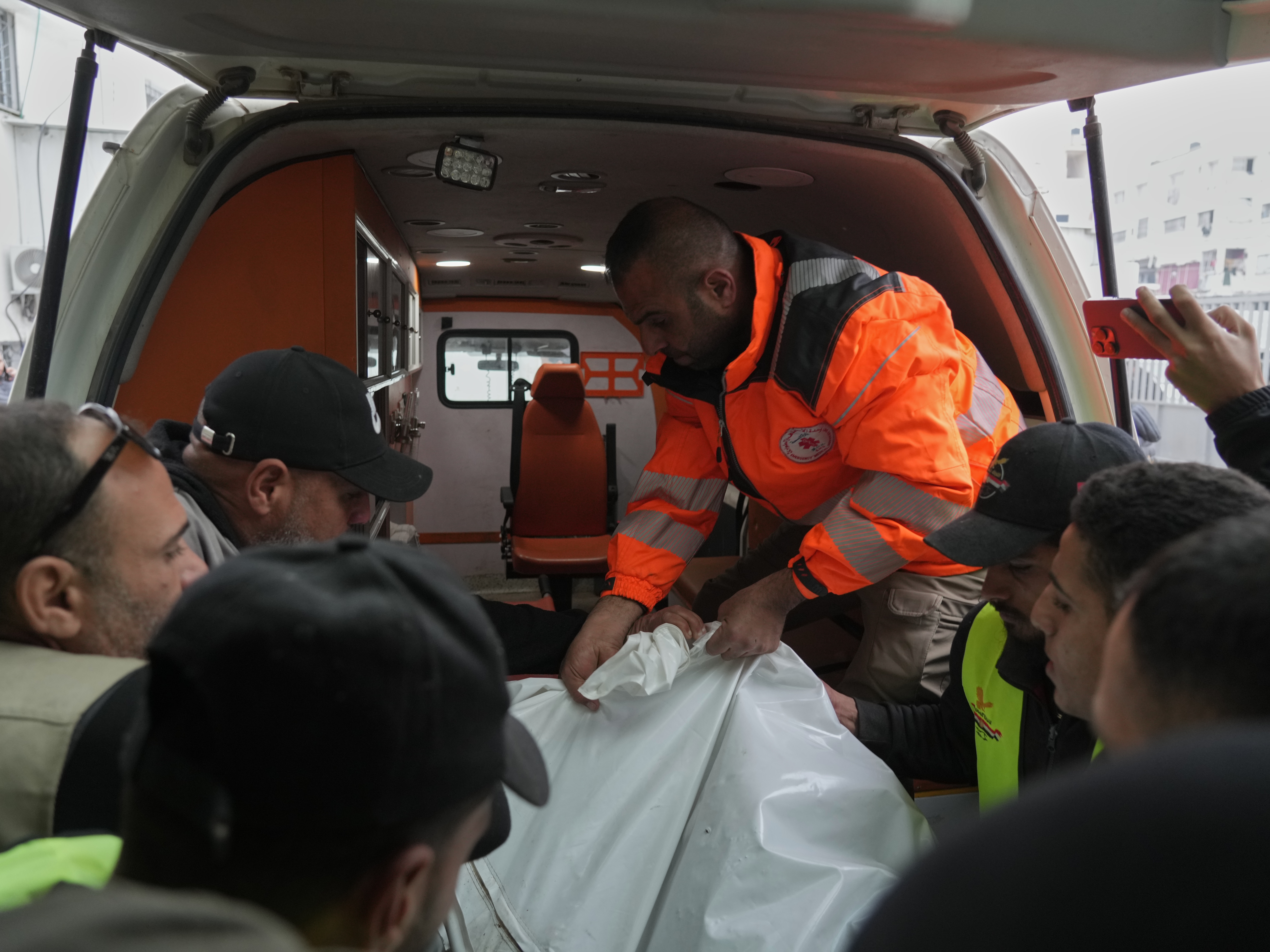 caption: People carry a bag containing the bodies of the Palestinian journalists Abd Shaat and Mohamed Qeshta, who were killed in an Israeli strike on a vehicle, before their funeral at Shifa Hospital, in Gaza City, Wednesday, Jan. 21, 2026.