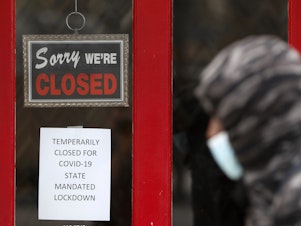caption: A pedestrian walks by a closed shop in Grosse Pointe, Mich., on Thursday. The Labor Department is expected to report on Friday that the U.S. lost millions of jobs last month because of the coronavirus pandemic.