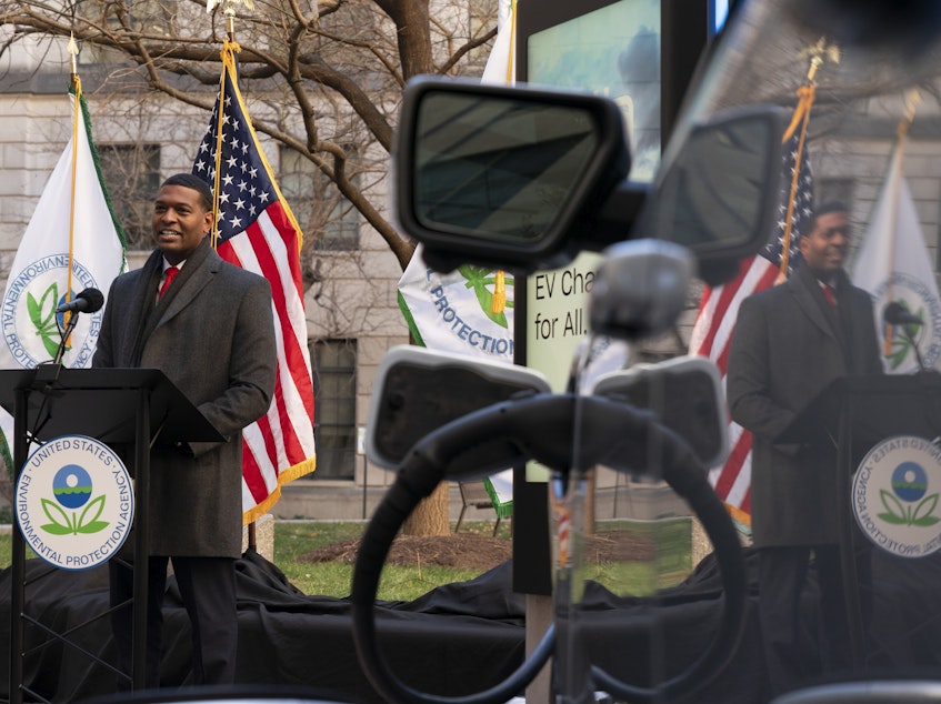 caption: Environmental Protection Agency Administrator Michael Regan is reflected in an electronic vehicle as it charges as he speaks during an event to announce a final rule for federal greenhouse gas emissions standards for cars and trucks on Monday.
