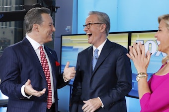 caption: Fox News has fired former anchor Ed Henry, left, who is standing with co-hosts Steve Doocy and Ainsley Earhardt on the "Fox & friends" television program in September 2019. (AP Photo/Richard Drew)