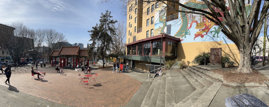 caption: Hing Hay Park is a center of activity in the C-ID. People play ping pong on stone tables, while partners move chess pieces on nearby benches.