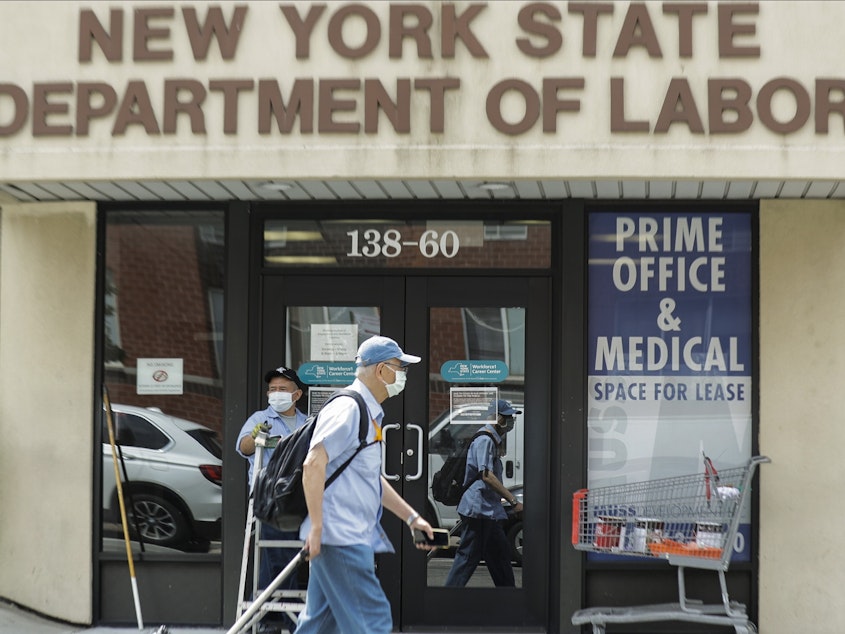 caption: Pedestrians pass a New York State Department of Labor office June 11 in Queens. The Federal Reserve expects the U.S. unemployment rate to still be more than 9% by the end of 2020.