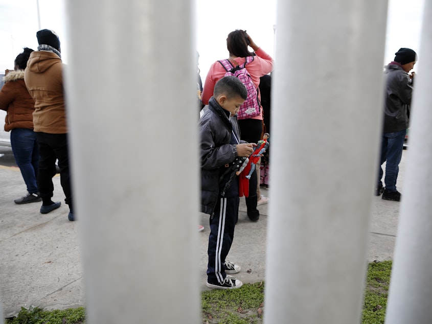 caption: A migrant family waits in Tijuana, Mexico, before being transported to the San Ysidro port of entry to begin the process of applying for asylum in the United States. A new Trump administration rule says Central American migrants who pass through a third country en route to the U.S. cannot apply for asylum at the U.S. southern border.