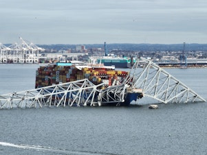 caption: A steel frame from the collapsed Francis Scott Key bridge in Baltimore covers the top of the Dali ship. The container ship crashed into the bridge on Tuesday.