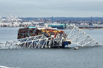caption: A steel frame from the collapsed Francis Scott Key bridge in Baltimore covers the top of the Dali ship. The container ship crashed into the bridge on Tuesday.