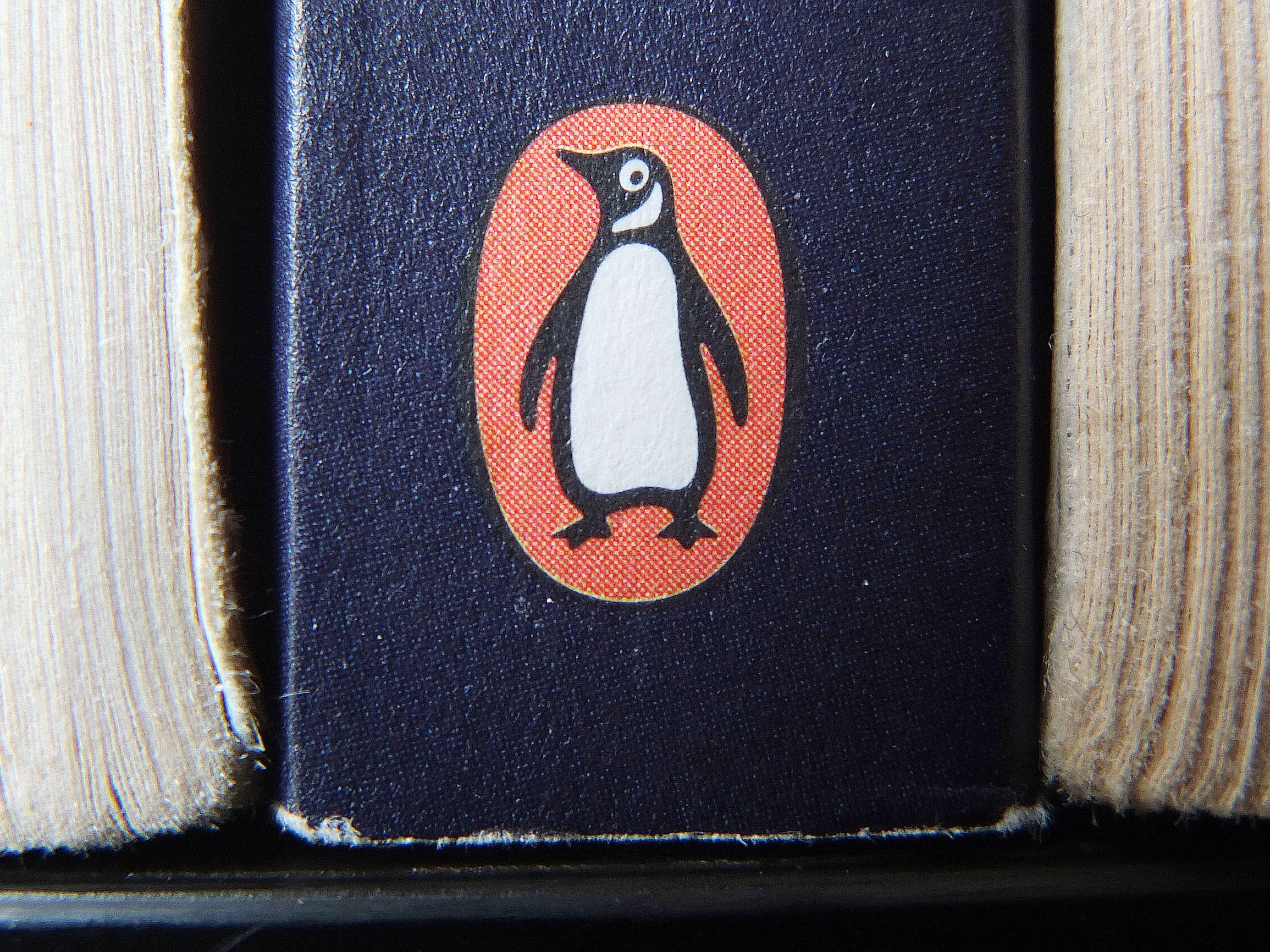 caption: The Penguin logo is visible on the spine of a book. The U.S. Department of Justice is suing Penguin Random House and Simon & Schuster to block the companies from completing a merger valued at $2.175 billion.