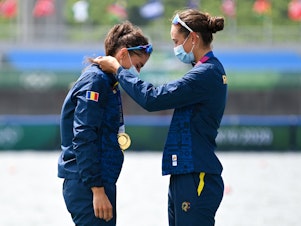 caption: Gold medalists Romania's Ancuta Bodnar and Simona Radis celebrate on the podium following the women's double sculls final during the Tokyo 2020 Olympic Games at the Sea Forest Waterway in Tokyo on July 28, 2021.