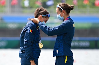 caption: Gold medalists Romania's Ancuta Bodnar and Simona Radis celebrate on the podium following the women's double sculls final during the Tokyo 2020 Olympic Games at the Sea Forest Waterway in Tokyo on July 28, 2021.