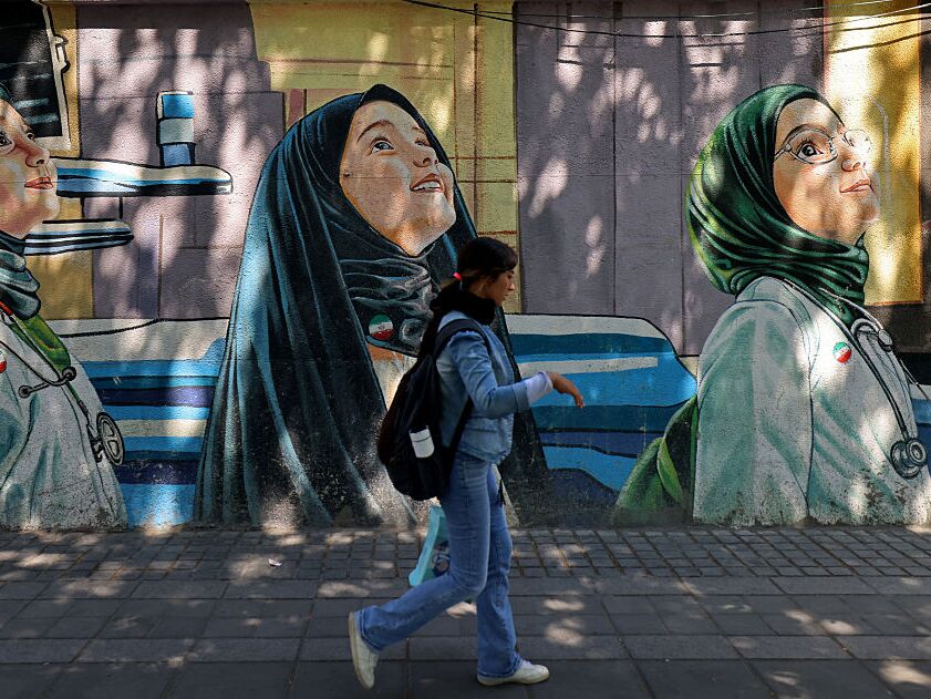 caption: A woman walks past a wall mural along the roadside in Tehran on Sunday.