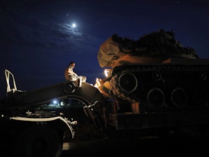 caption: A Turkish army officer prepares to unload a tank from a truck to its new position on the Turkish side of the border between Turkey and Syria, in Sanliurfa province, southeastern Turkey, on Tuesday.