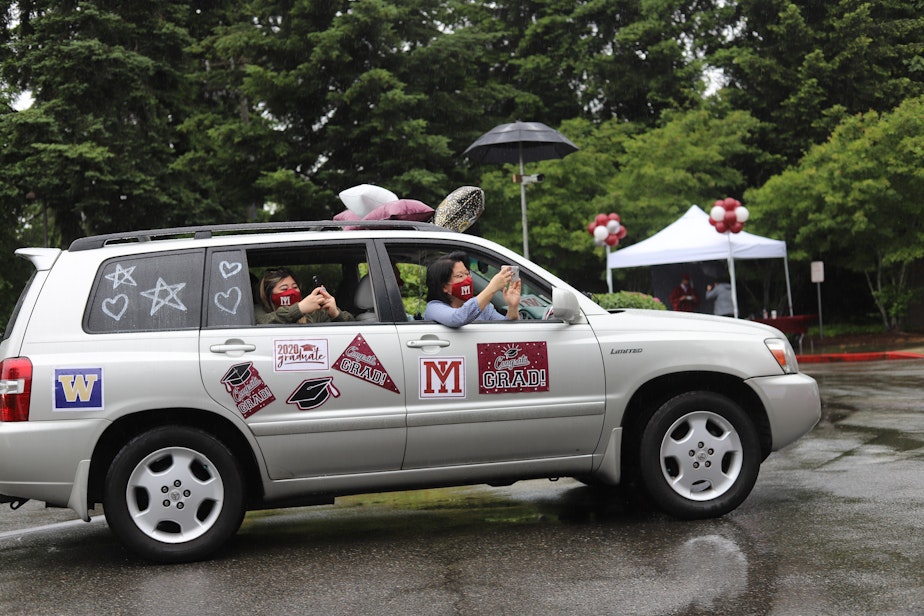 caption: Lauren Louie, left, and Amy Maeda, right, lean out their decorated car to photograph senior Nicole Hibi graduating on stage on June 9, 2020. With the drive-through graduation came the opportunity to recognize seniors with personalized, and sometimes extravagant, decor. Trends included chalk paint, balloons and photo prints.