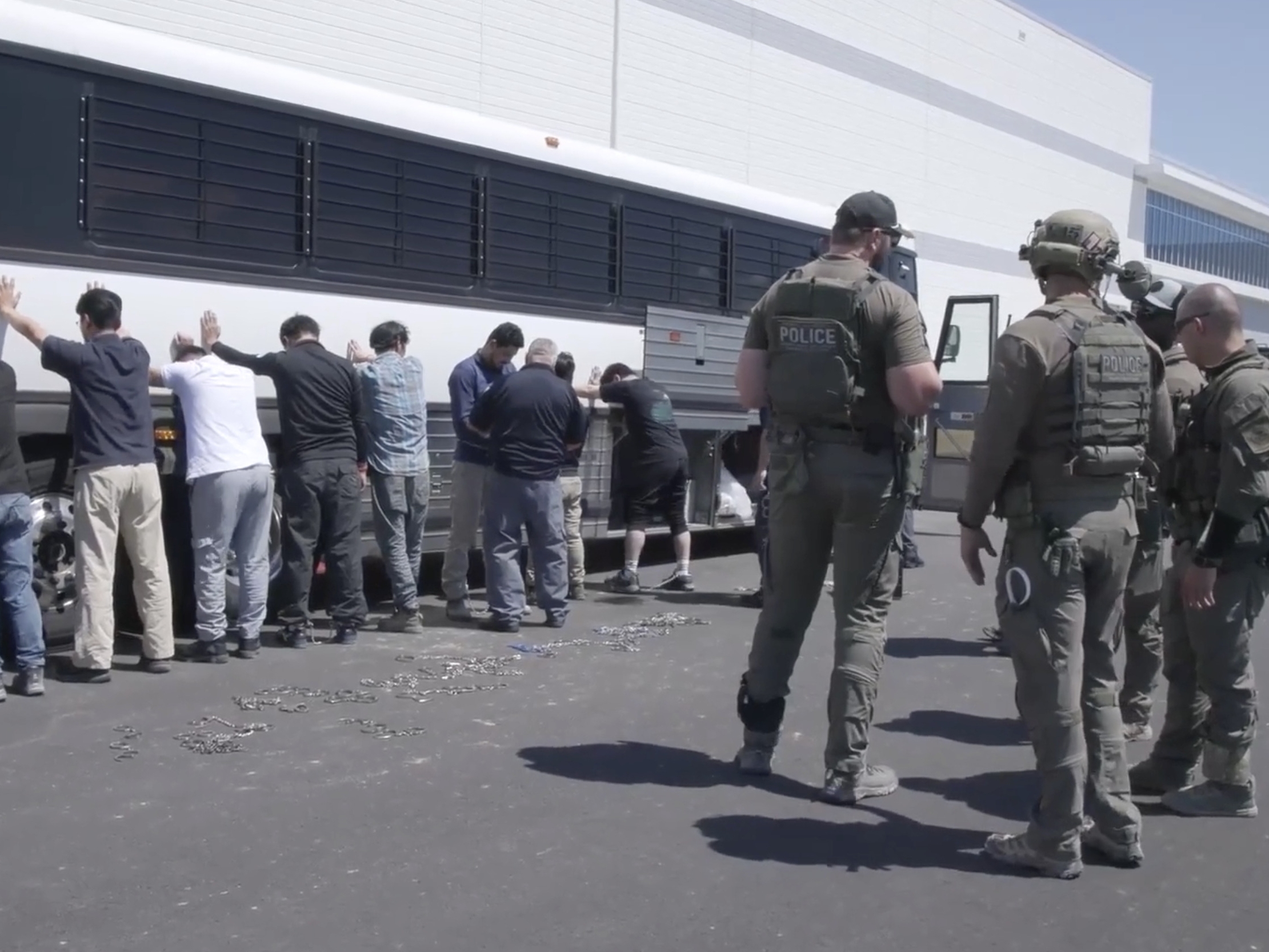 caption: This image from video provided by U.S. Immigration and Customs Enforcement via DVIDS shows manufacturing plant employees waiting to have their legs shackled at the Hyundai Motor Group's electric vehicle plant, Thursday, Sept. 4, 2025, in Ellabell, Ga.