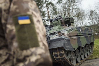 caption: A Ukrainian soldier stands in front of a Marder infantry fighting vehicle at the German forces Bundeswehr training area in Munster, Germany, on Feb. 20, 2023.