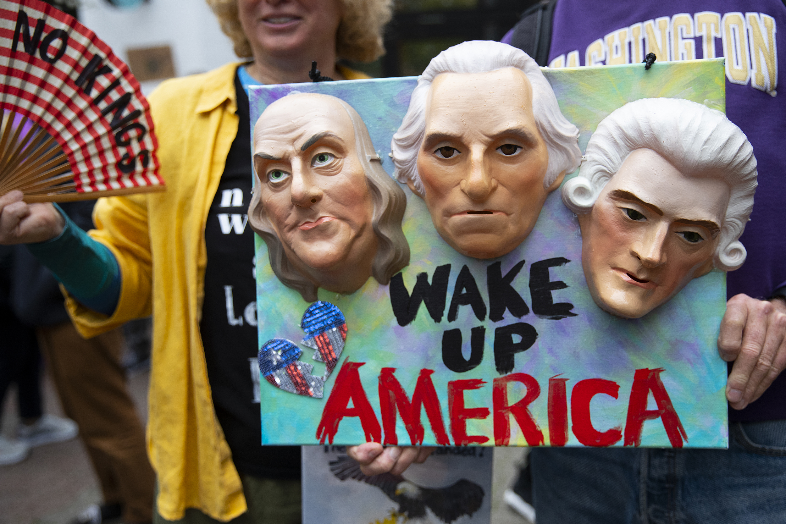 caption: ‘Wake Up America’ reads a protesters sign ahead of the No Kings rally and march on Saturday, October 18, 2025, at Seattle Center. 