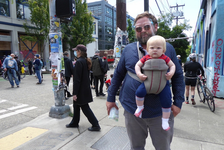 caption: Gabe Magic, and his 8-month-old Tilden, at the Capitol Hill Autonomous Zone, or CHAZ, in Seattle on June 11, 2020. Magic got his face shield from the Post Office; it was Tilden's first time in the area. They live about eight blocks away. 