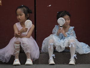 caption: Children cool themselves with electric fans in Beijing on June 25, 2023. The National Oceanic and Atmospheric Administration says this was the hottest June on record globally.