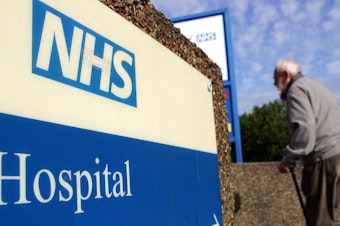 caption: A man walks past a National Health Service sign in 2007 in London. The NHS offers services at the Askern Medical Practice in Doncaster, whose patients mistakenly received text messages informing them of a terminal cancer diagnosis.