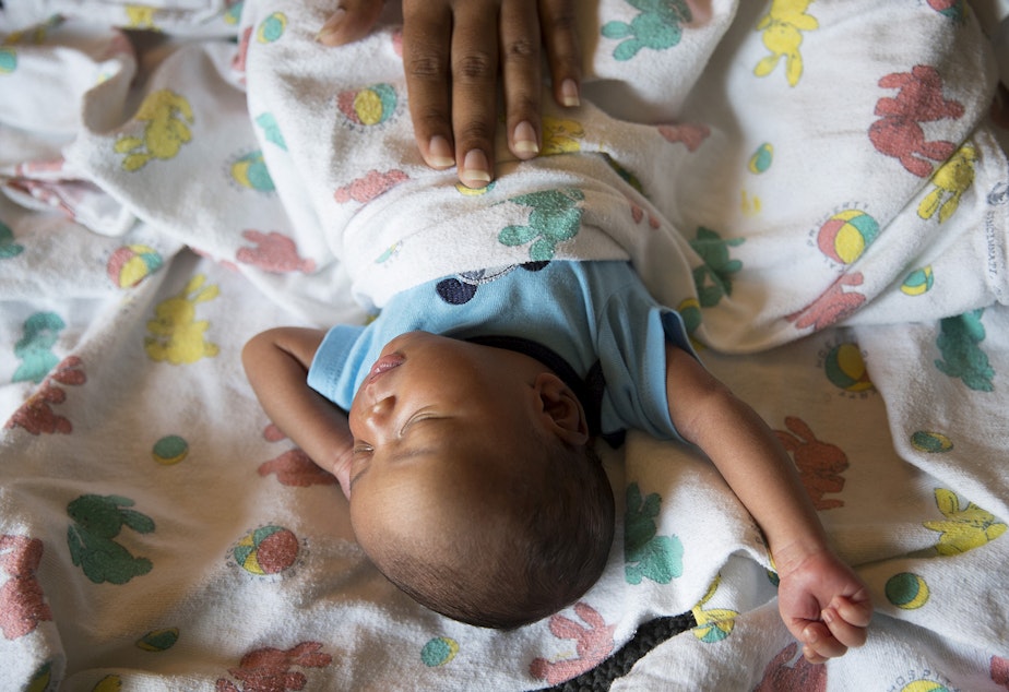 caption: Tiffany Hicks places her hand on her newborn son Elijah as he sleeps on Sunday, September 3, 2017, in their room at Mary's Place, a homeless shelter for families, in Seattle.