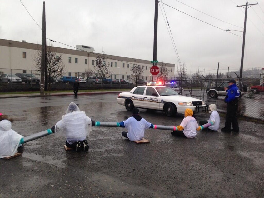 caption: A dozen protesters block the entrance to the Northwest Detention Center in Tacoma in February 2014. Deportations from the Northwest have declined by nearly half, but now a larger proportion of deportees have a clean record.