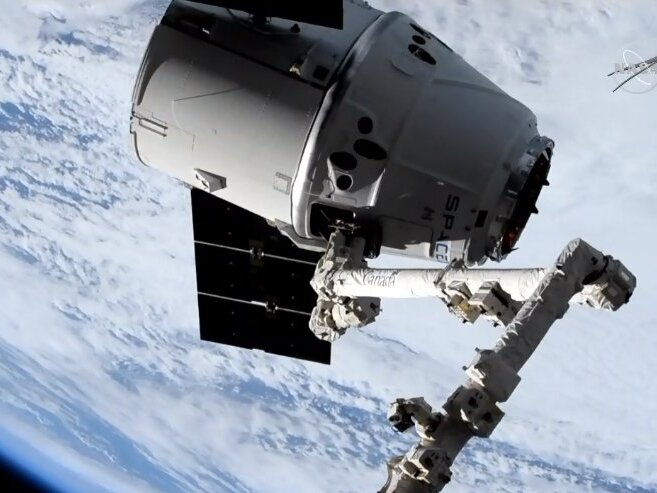 caption: A robotic arm attached to the International Space Station brings in the spacecraft carrying one of two Orbiting Carbon Observatory instruments, known as OCO-3, in 2019. NASA has put out a call for private groups to potentially take over the cost of maintaining the instrument, which measures carbon dioxide in Earth's atmosphere.