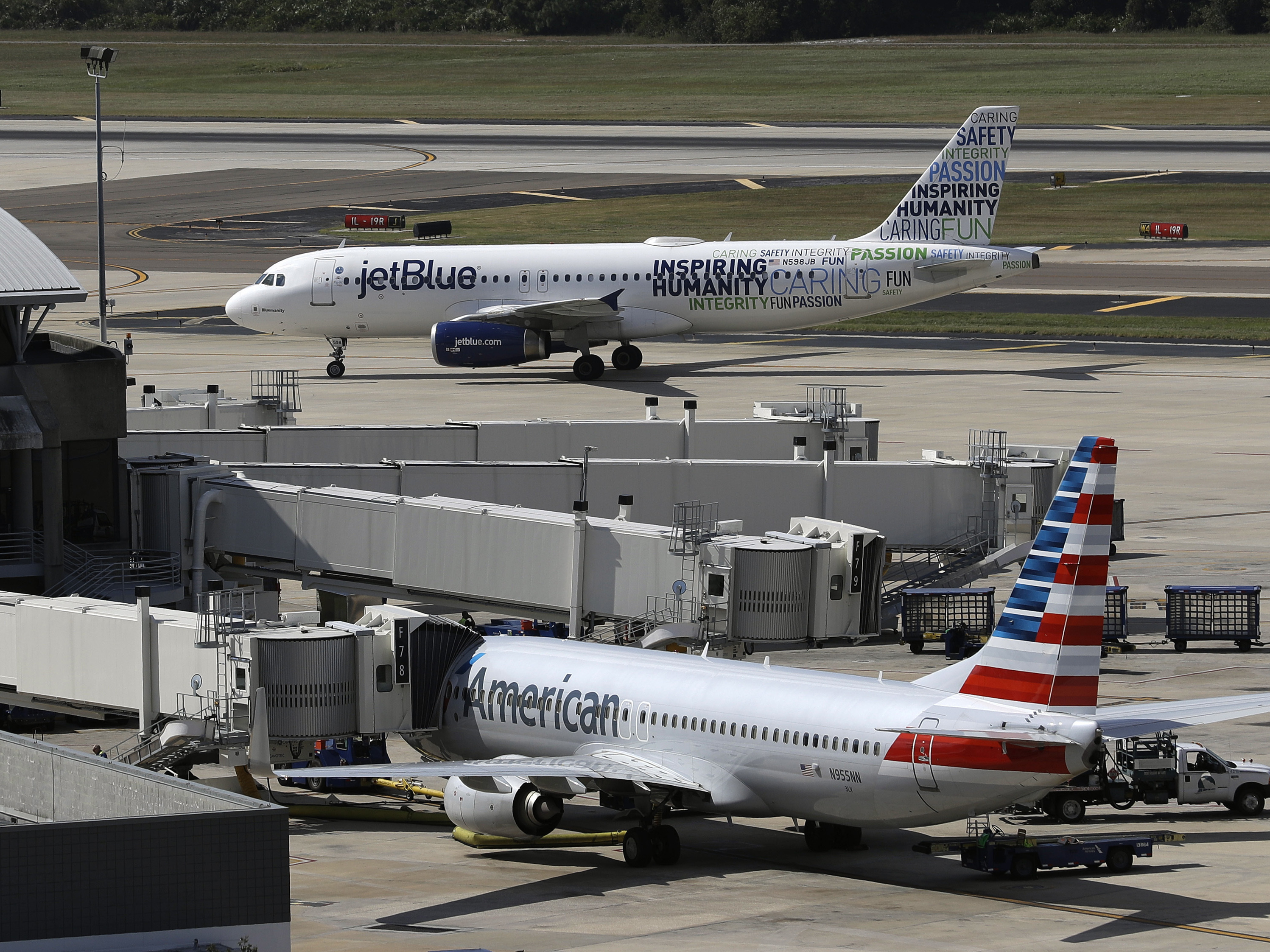 caption: A JetBlue Airbus A320 taxis to a gate on Oct. 26, 2016, after landing, as an American Airlines jet is seen parked at its gate at Tampa International Airport in Tampa, Fla.
