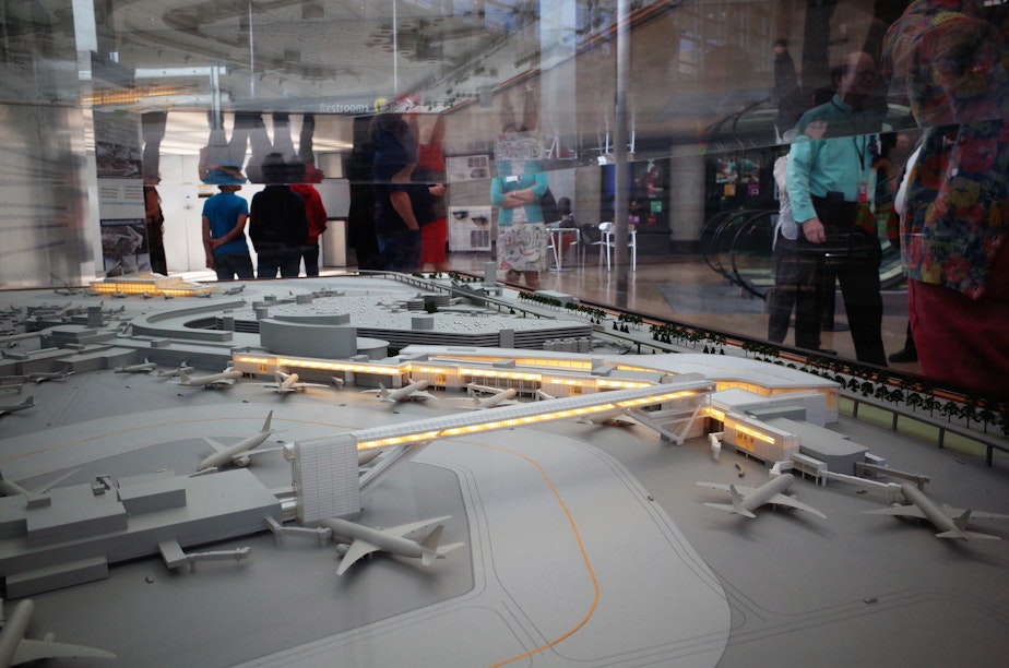 caption: Sea-Tac visitors pass a model of the International Arrivals Terminal, to be completed in 2019. 