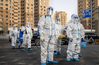 caption: Workers wear protective gear in a Beijing neighborhood placed under lockdown in November. China had raised hopes by slightly relaxing its zero-COVID policy, but cities have been contending with a surge in cases.
