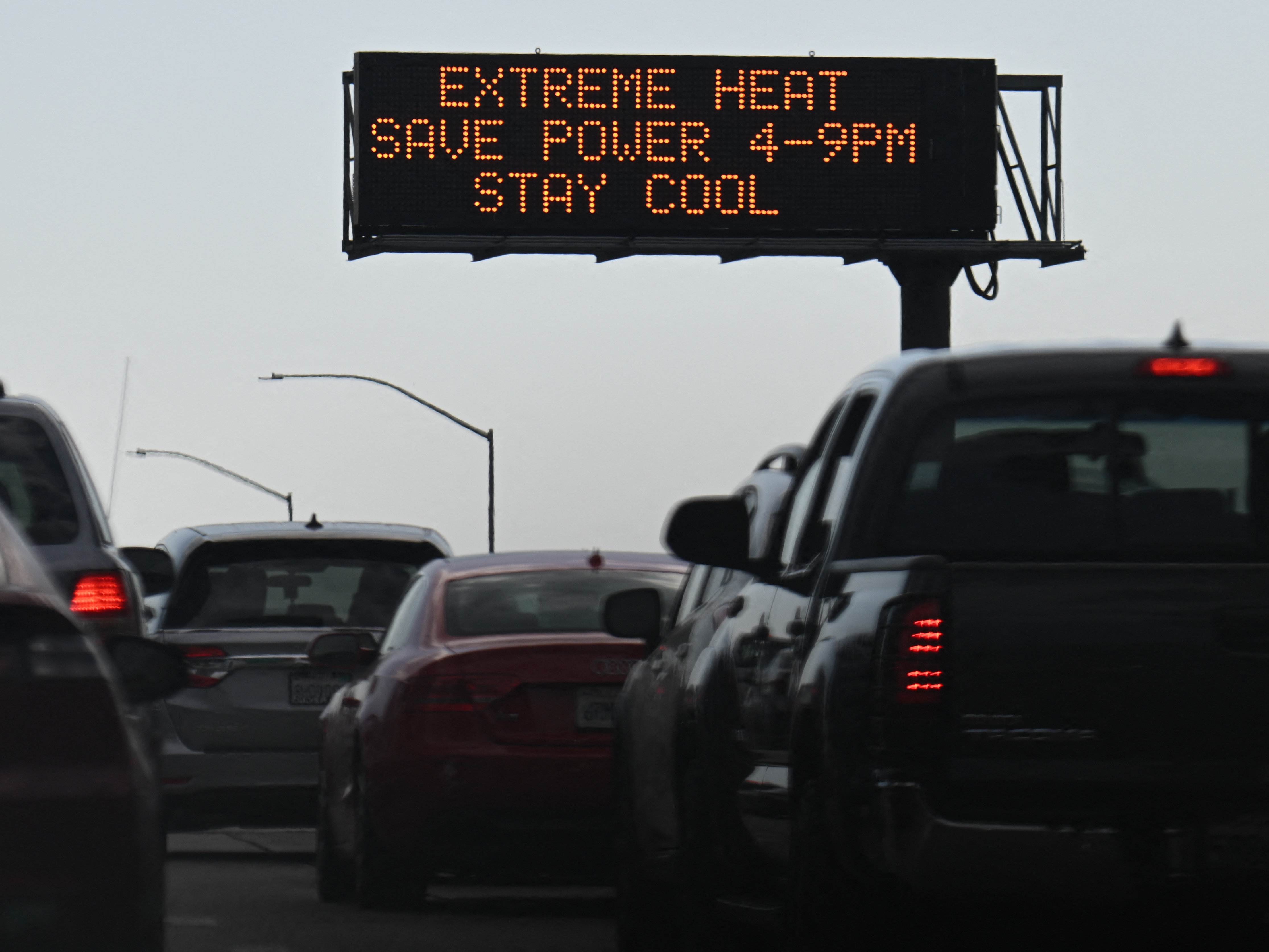 caption: Vehicles drive past a sign on the 110 Freeway warning of extreme heat and urging energy conservation during a heat wave in downtown Los Angeles on Sept. 2. Soaring electricity bills are pinching many household budgets across the country even as gasoline prices have come down.