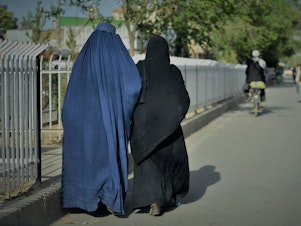caption: Women wearing a burqa (L) and a Niqab (R) walk along a street in Kabul on May 7, 2022.