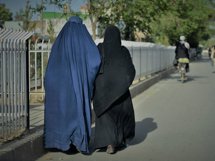 caption: Women wearing a burqa (L) and a Niqab (R) walk along a street in Kabul on May 7, 2022.