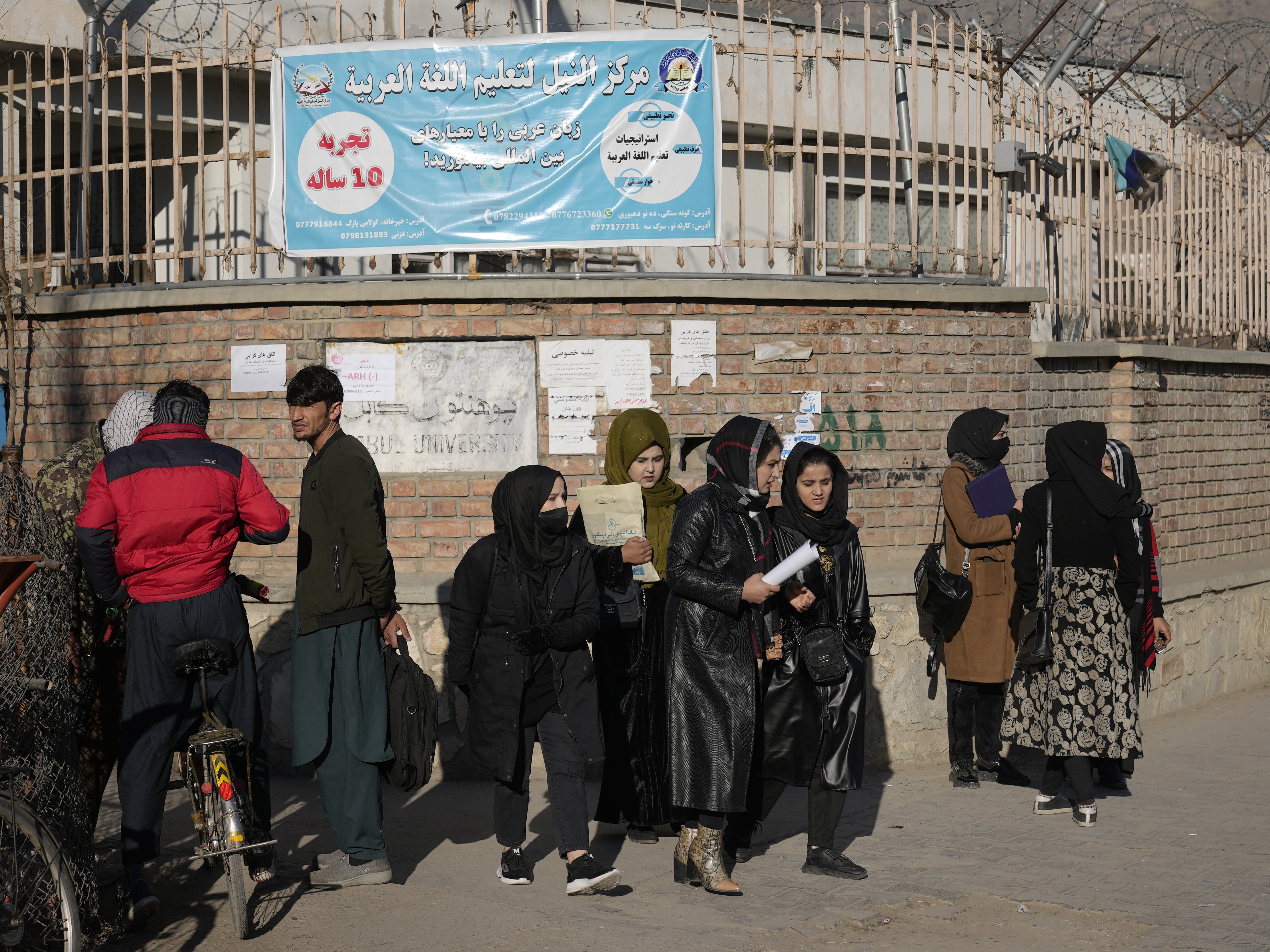 caption: Women students stand outside Kabul University in Afghanistan. As of December 2022, the Taliban has banned women from higher education. But for some, a USAID grant provided online options as well as a chance to study abroad. That scholarship program has now been terminated.