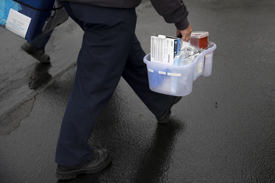 caption: Puget Sound Regional Firefighter Nikki Smith carries supplies back to the fire truck after vaccinating Connie Palmer against Covid-19 at her home, on Monday, May 24, 2021, in Kent.