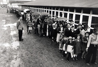 caption: Waiting in line at the mess hall, 1942, Puyallup Assembly Center, Washington State. 